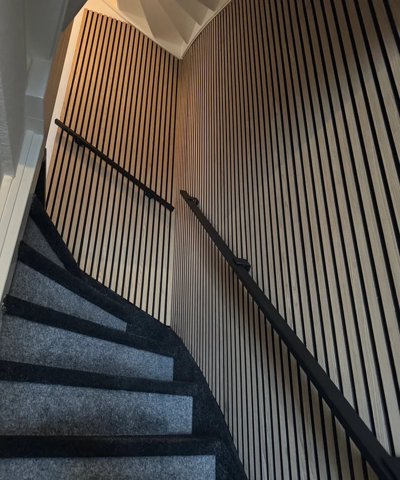 Modern staircase with gray carpeted steps and black metal handrail against corrugated metal walls with natural light