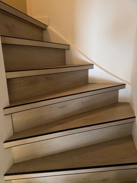 Staircase with wooden steps and black metal edge trim, photographed from above in an interior space with white walls