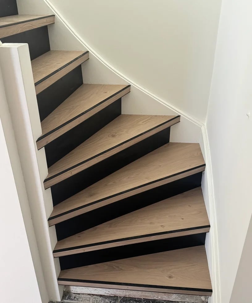 Modern staircase with light wood steps and black risers ascending against white walls, viewed from below