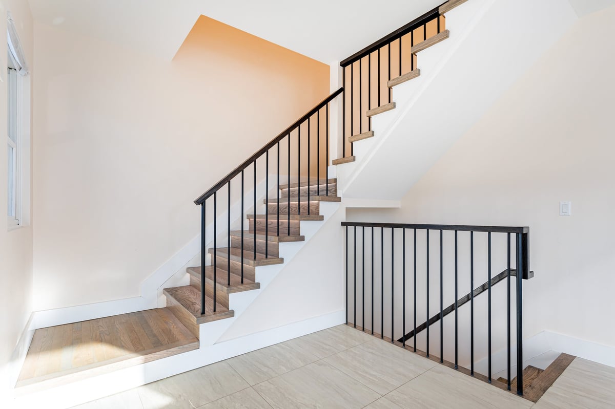 Modern staircase with black metal railing and wooden steps in a minimalist interior with white walls
