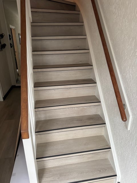 Wooden staircase with white walls and dark railings viewed from top looking downward