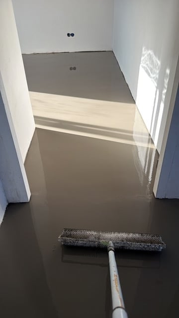 A hallway under construction with white walls, partially painted flooring, and a mop with dark floor in the foreground