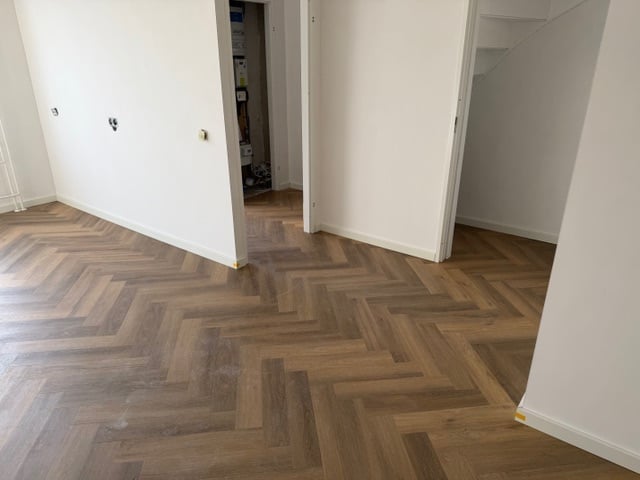 Empty room with herringbone wood flooring, white walls, and open doorways leading to adjacent rooms