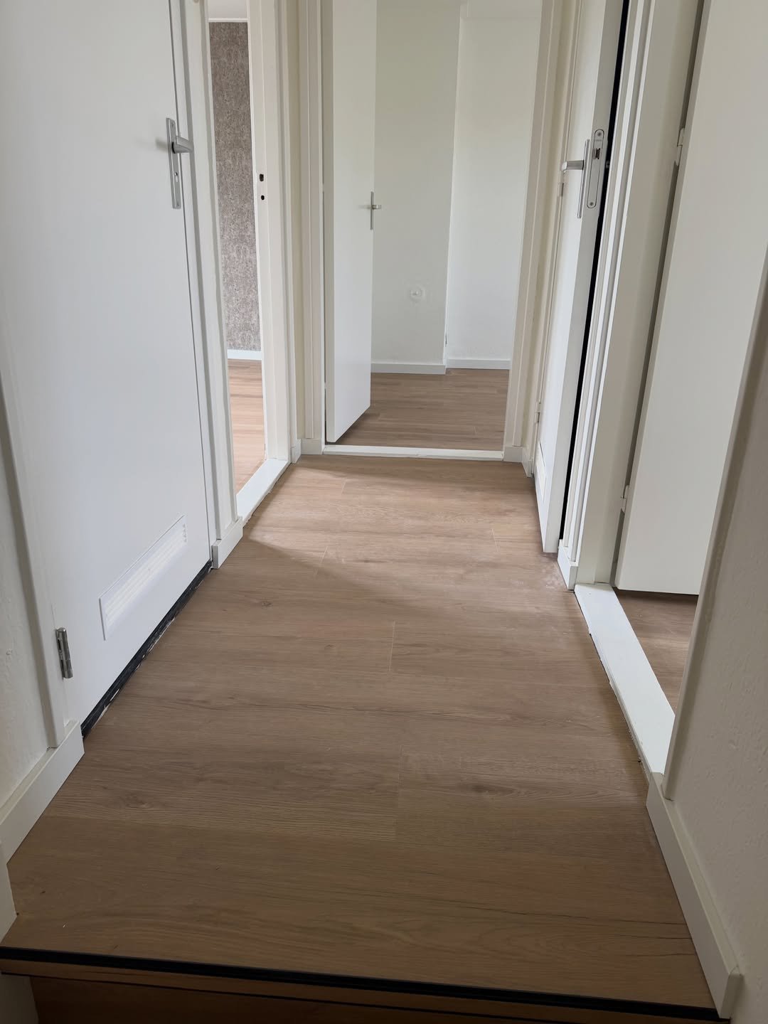 Long residential hallway with hardwood flooring, white walls, and multiple white doors on both sides