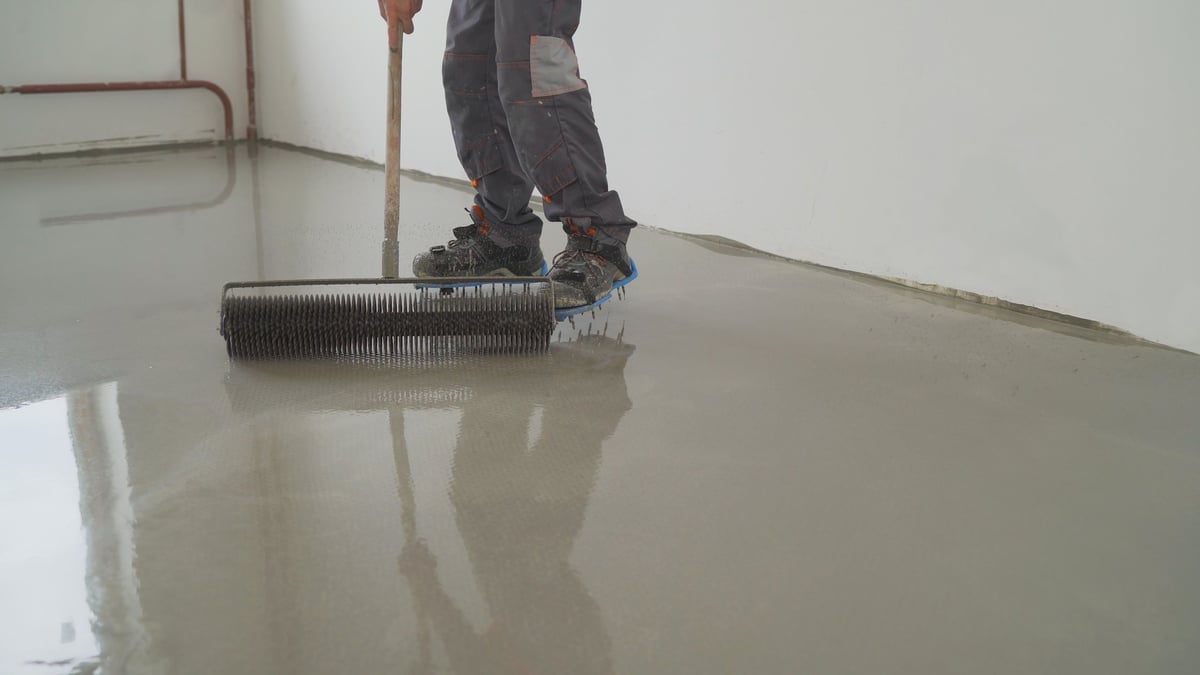 Worker smoothing wet concrete floor with a long-handled trowel in an indoor construction area