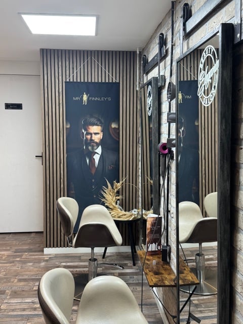 Modern salon interior with white chairs, black framed mirror, decorative gold wheat arrangement, and large portrait poster of a man in business attire