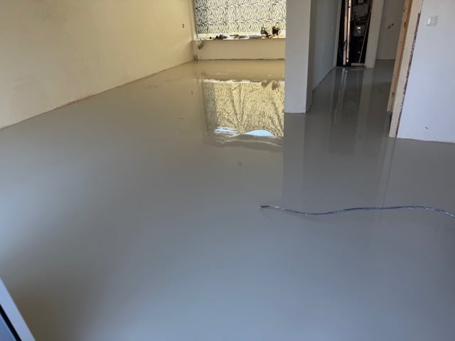 Empty concrete floor in an unfinished interior space with windows and doorways visible